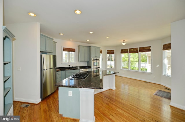 kitchen featuring a sink, light wood-type flooring, stainless steel appliances, baseboards, and a kitchen island