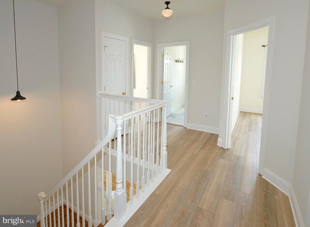 corridor with baseboards, light wood-style floors, and an upstairs landing