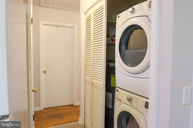 clothes washing area with wood finished floors, attic access, water heater, stacked washer and clothes dryer, and laundry area
