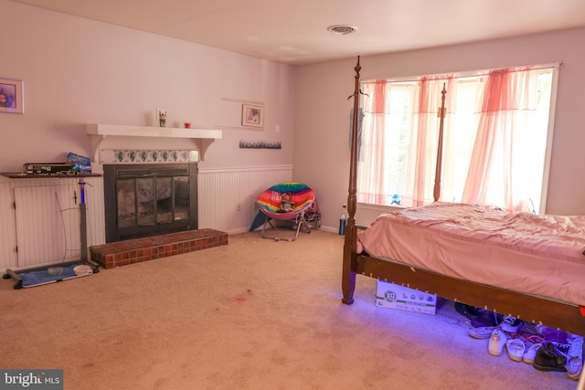 carpeted bedroom featuring a tile fireplace, visible vents, and wainscoting