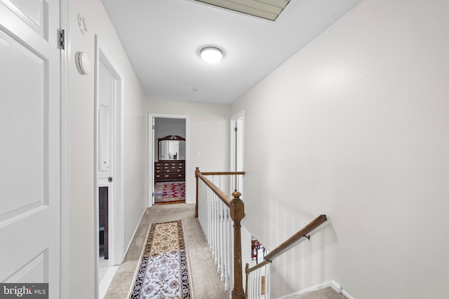 hall featuring an upstairs landing, light colored carpet, and baseboards