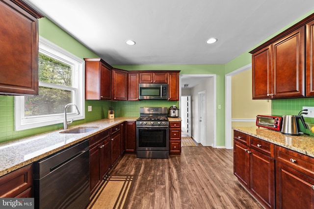 kitchen featuring light stone countertops, a sink, stainless steel appliances, tasteful backsplash, and dark wood finished floors