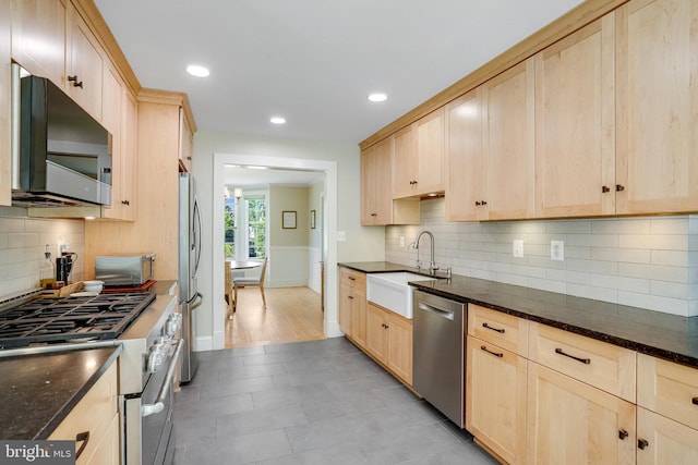 kitchen featuring a sink, light brown cabinets, stainless steel appliances, and dark stone countertops