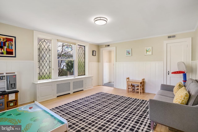 living area featuring visible vents, crown molding, wainscoting, radiator, and wood finished floors