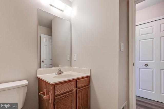half bath featuring wood finished floors, visible vents, vanity, and toilet