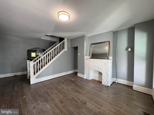 unfurnished living room featuring arched walkways, baseboards, wood finished floors, and stairway