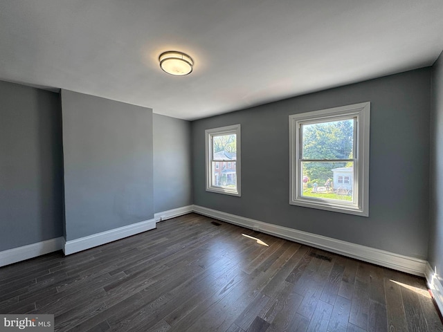 unfurnished room with baseboards, dark wood-style flooring, and visible vents