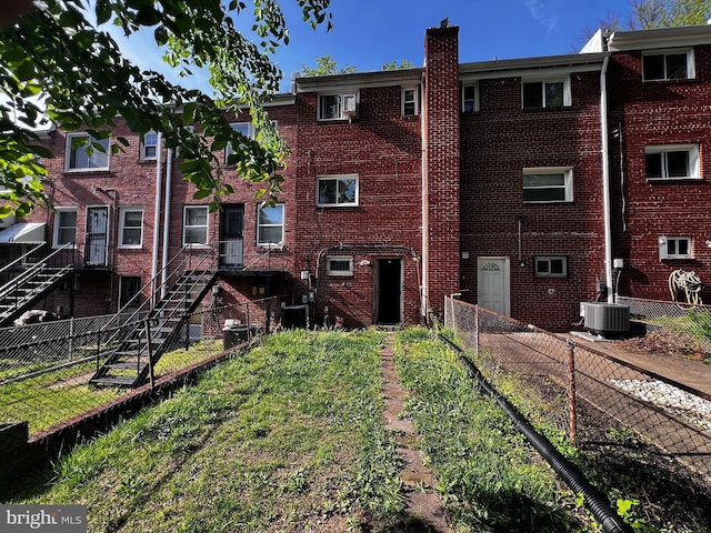 rear view of property featuring brick siding, a chimney, central AC unit, and a fenced backyard