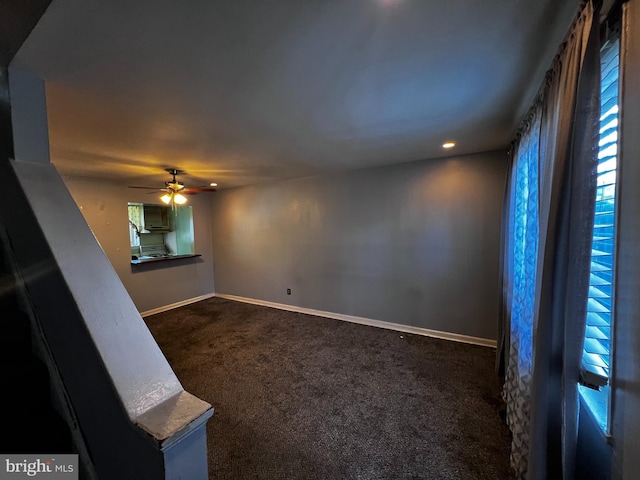 interior space featuring a ceiling fan, baseboards, a healthy amount of sunlight, and dark colored carpet