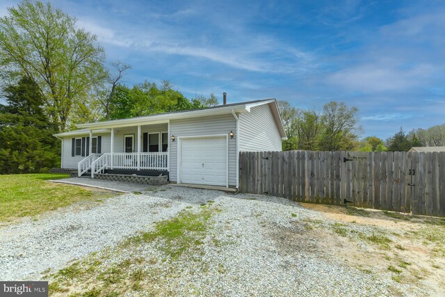 single story home featuring fence, covered porch, gravel driveway, and an attached garage