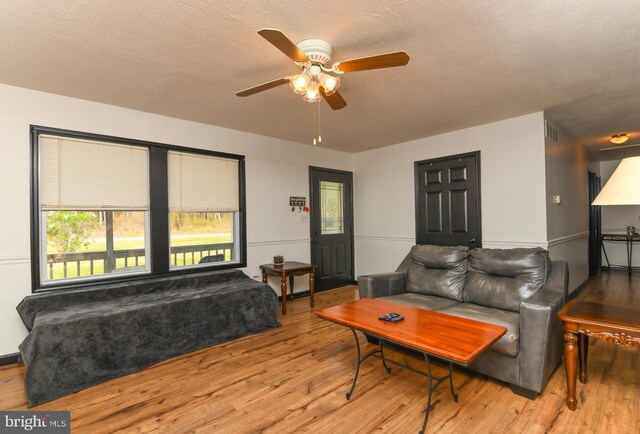 living area featuring a textured ceiling, wood finished floors, a ceiling fan, and visible vents