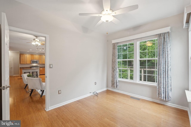 empty room with ceiling fan, light wood-style flooring, and baseboards
