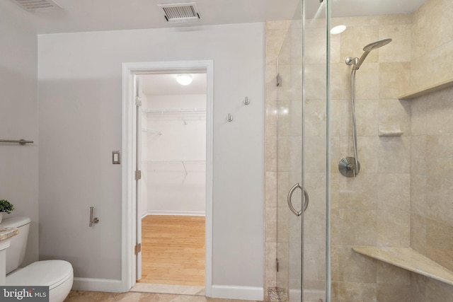 bathroom with a stall shower, toilet, a walk in closet, and baseboards