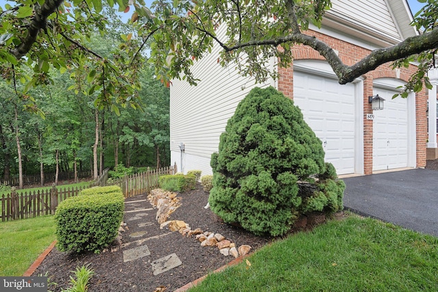 view of home's exterior with fence, brick siding, driveway, and a garage