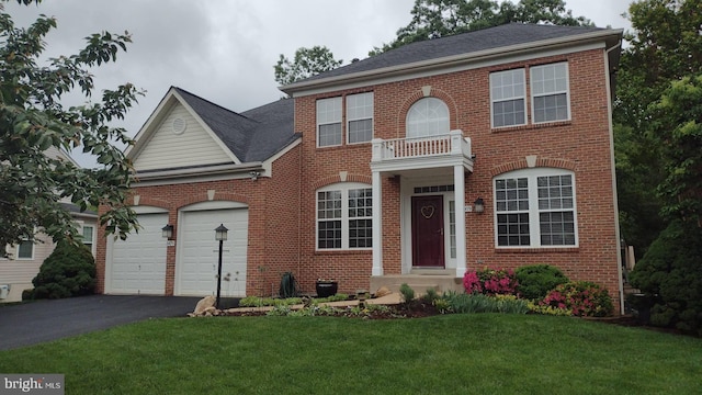 colonial house with brick siding, driveway, an attached garage, a front yard, and a shingled roof