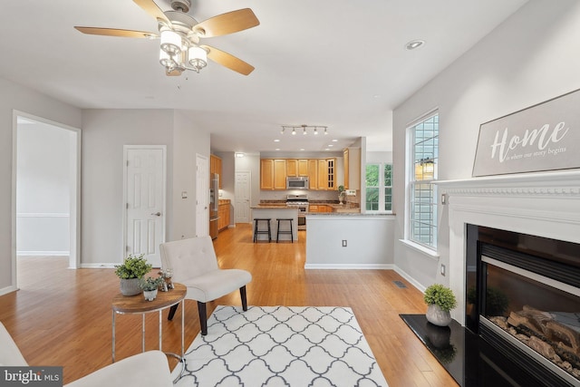 living room with light wood-style flooring, a glass covered fireplace, baseboards, ceiling fan, and recessed lighting