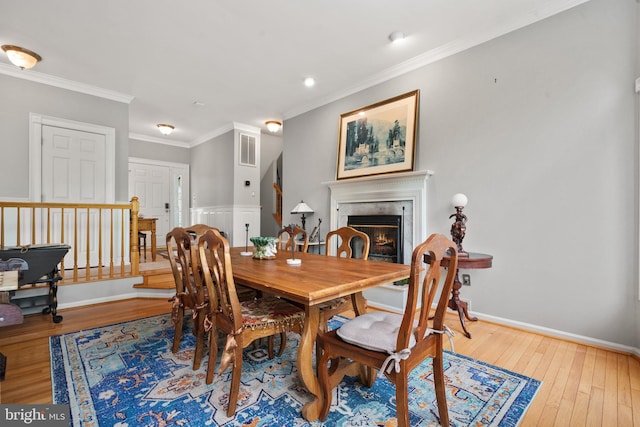 dining space featuring hardwood / wood-style flooring, visible vents, baseboards, a glass covered fireplace, and ornamental molding