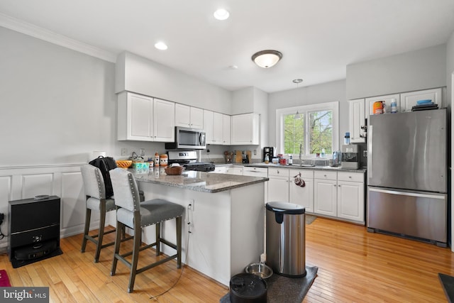 kitchen with appliances with stainless steel finishes, white cabinetry, a peninsula, and a breakfast bar area