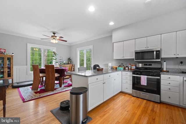 kitchen with white cabinets, stainless steel appliances, a peninsula, and ornamental molding