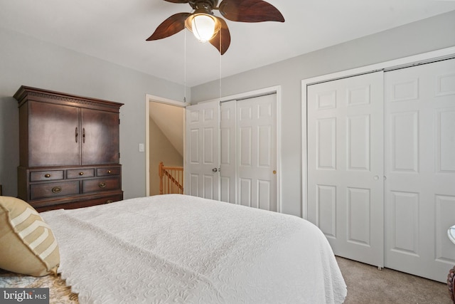 bedroom with light colored carpet, ceiling fan, and multiple closets