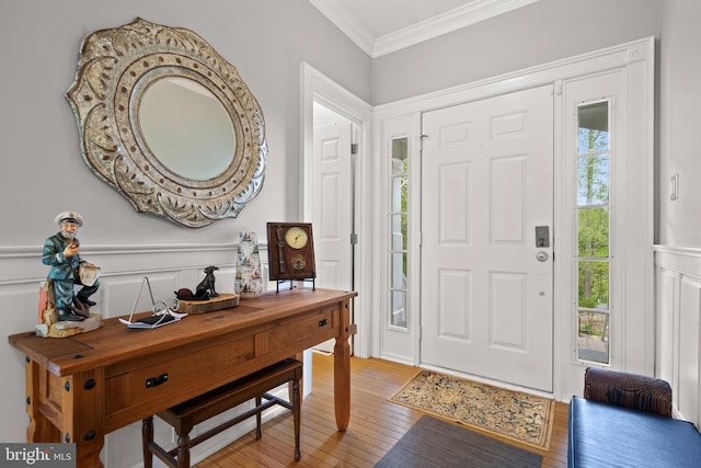 foyer entrance with a decorative wall, light wood-type flooring, ornamental molding, and wainscoting