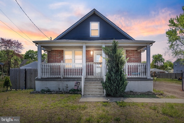 bungalow featuring fence, a porch, a front lawn, and brick siding
