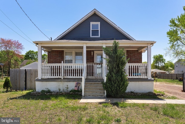 bungalow with covered porch, brick siding, and fence