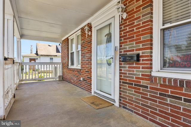 view of exterior entry featuring a porch and brick siding