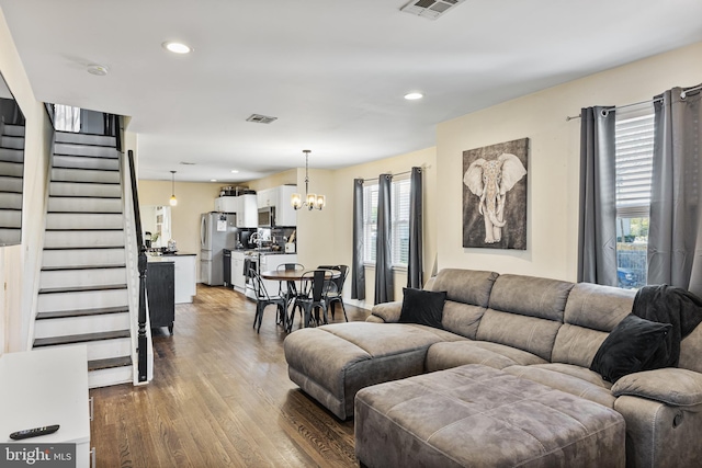 living room with stairway, visible vents, wood finished floors, and a notable chandelier