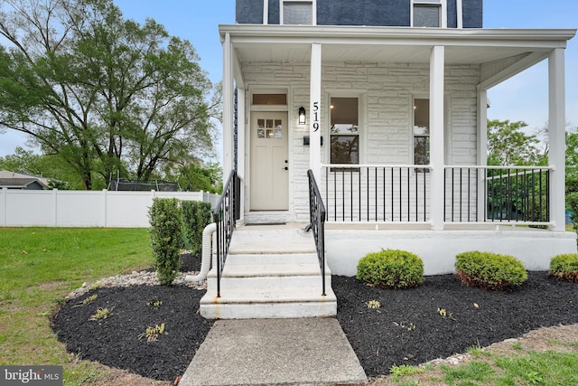 view of exterior entry with a yard, stone siding, covered porch, and fence