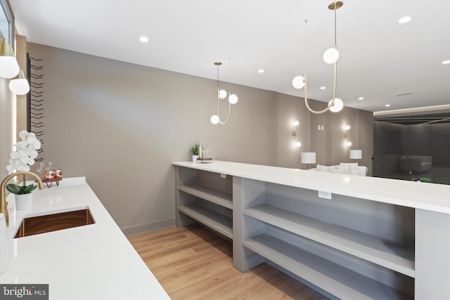 kitchen featuring open shelves, light countertops, a sink, light wood-style flooring, and hanging light fixtures