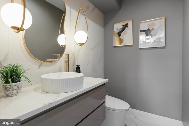 half bathroom featuring baseboards, marble finish floor, vanity, and toilet