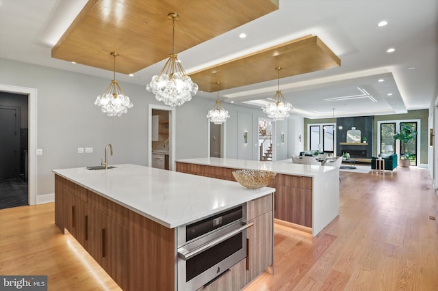 kitchen with brown cabinets, a large island with sink, an inviting chandelier, a tray ceiling, and modern cabinets