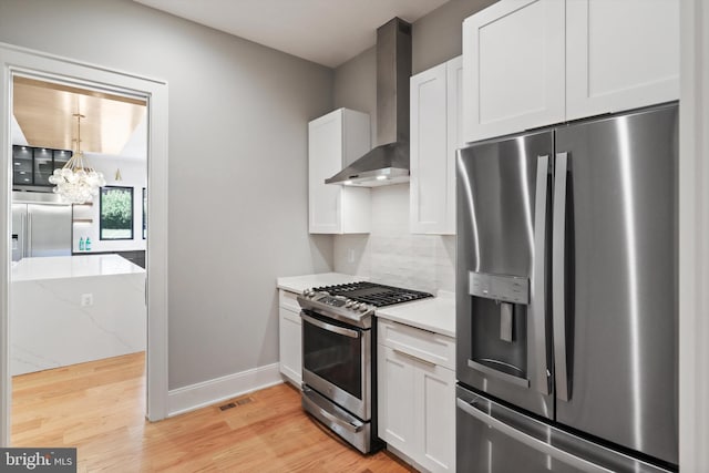 kitchen with wall chimney exhaust hood, light wood-style flooring, visible vents, a chandelier, and appliances with stainless steel finishes