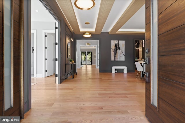 corridor featuring light wood finished floors, baseboards, and a tray ceiling