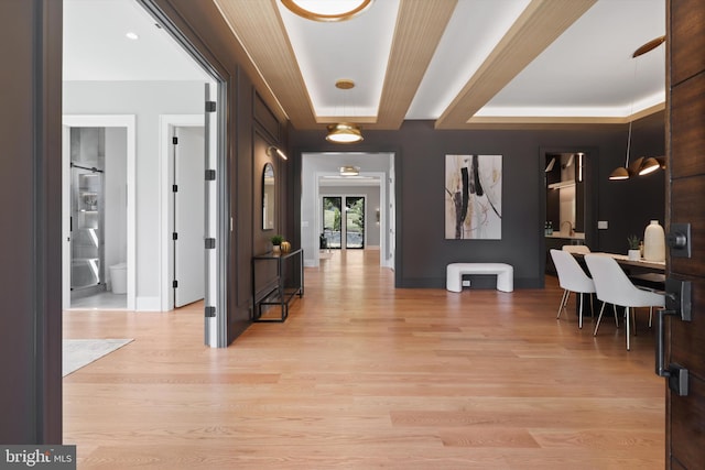 hall featuring a tray ceiling, light wood-type flooring, and baseboards