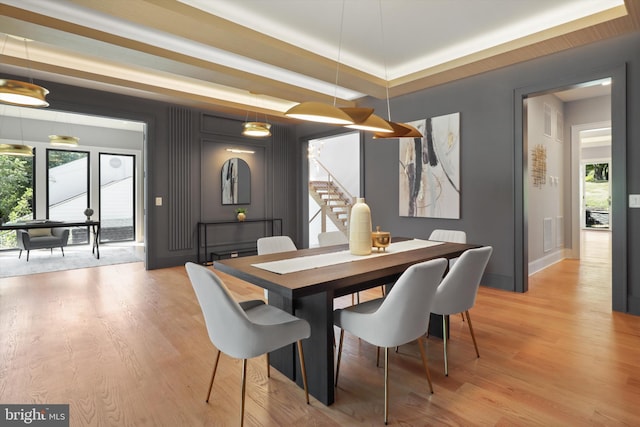 dining room with light wood finished floors, baseboards, visible vents, and stairs