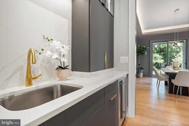 kitchen with a sink, beverage cooler, modern cabinets, pendant lighting, and light wood finished floors