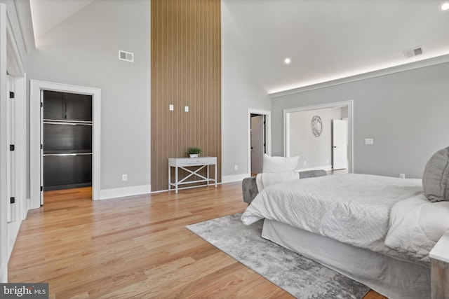 bedroom with a spacious closet, light wood-type flooring, visible vents, and high vaulted ceiling