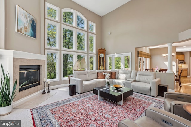 living area featuring ornate columns, a wealth of natural light, a tile fireplace, and a high ceiling