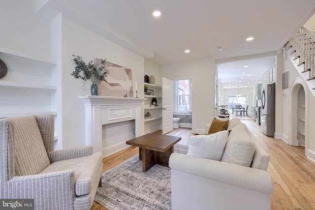living area with recessed lighting, light wood-style flooring, built in features, a glass covered fireplace, and baseboards