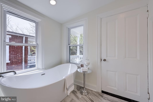 bathroom with a freestanding bath, marble finish floor, and baseboards