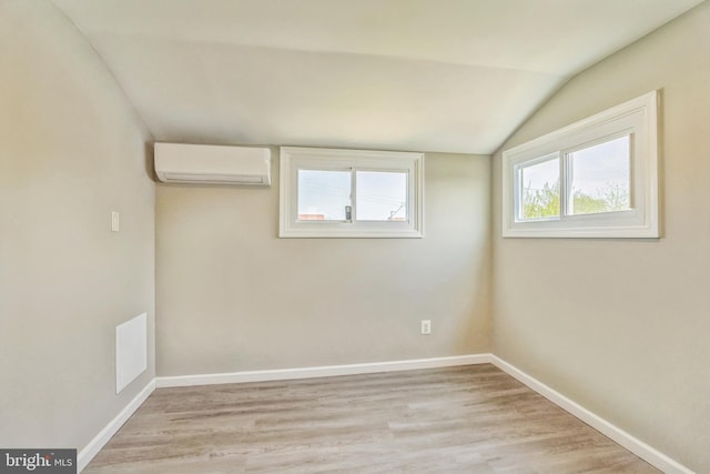 empty room with light wood-type flooring, a wall unit AC, vaulted ceiling, and baseboards
