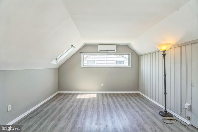 additional living space with an AC wall unit, vaulted ceiling with skylight, wood finished floors, and baseboards