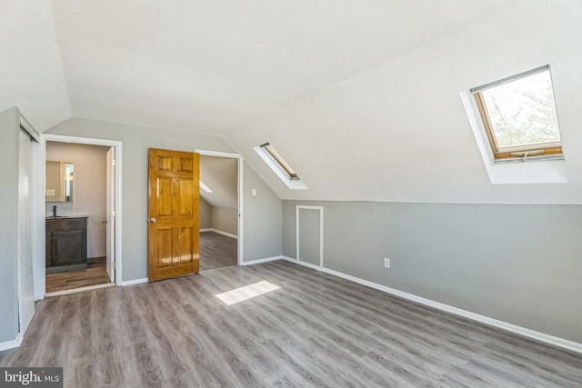 bonus room featuring lofted ceiling with skylight, wood finished floors, and baseboards