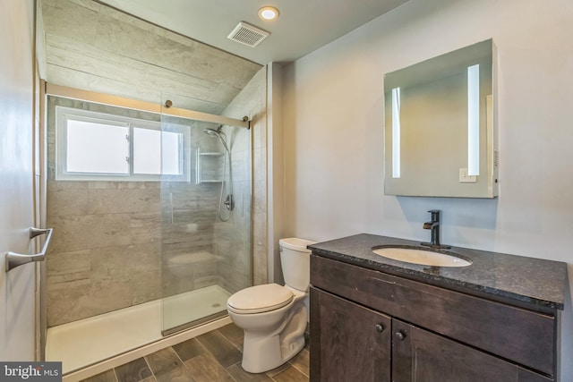 bathroom with tiled shower, vanity, toilet, visible vents, and wood finished floors