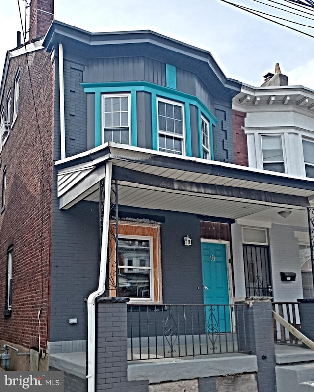 view of front facade with covered porch, a chimney, and brick siding