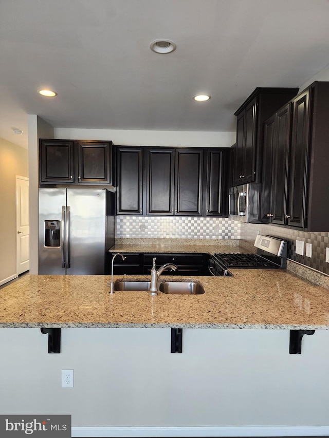 kitchen featuring light stone counters, dark cabinets, a breakfast bar, tasteful backsplash, and appliances with stainless steel finishes