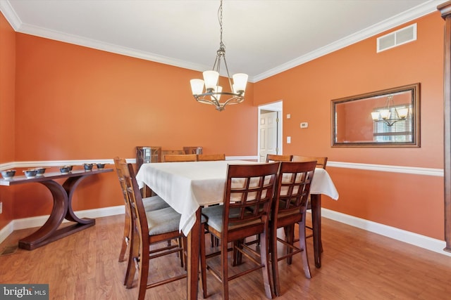 dining room with wood finished floors, visible vents, crown molding, and a chandelier