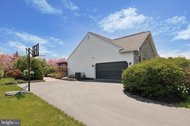 view of side of property featuring aphalt driveway, a garage, stone siding, central AC unit, and roof with shingles